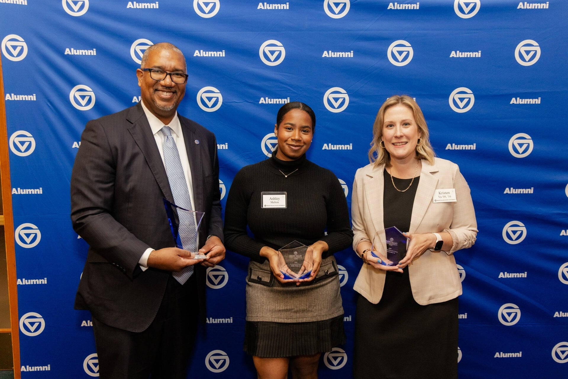 2026 Alumni Award winners pose with awards next to backdrop